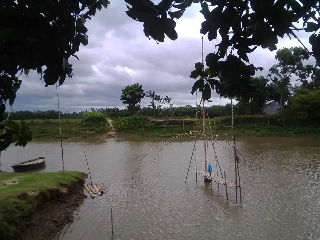 A wooden country boat moored at a quiet river landing under a grey sky.